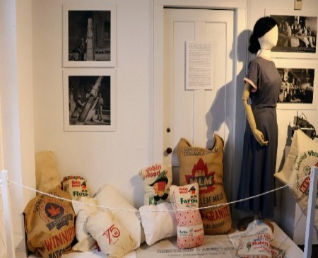 Various full flour bags with female mannequin in a grey dress and a sewing machine